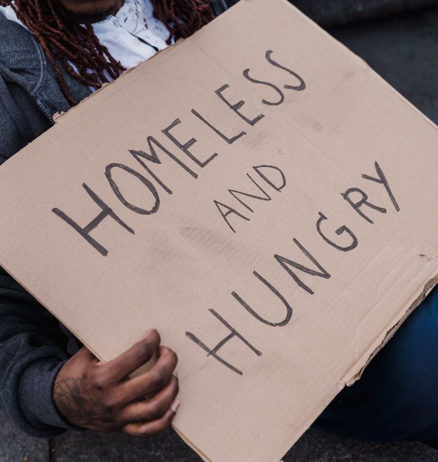 A person holding a cardboard sign that reads 'HOMELESS AND HUNGRY.'